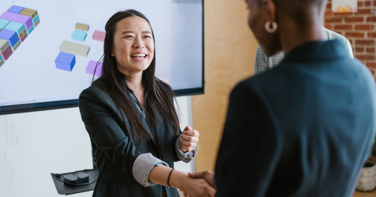 Black woman shaking hands with an Asian woman smiling